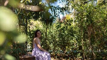A person sitting on a bench in a garden with dense foliage and trees.