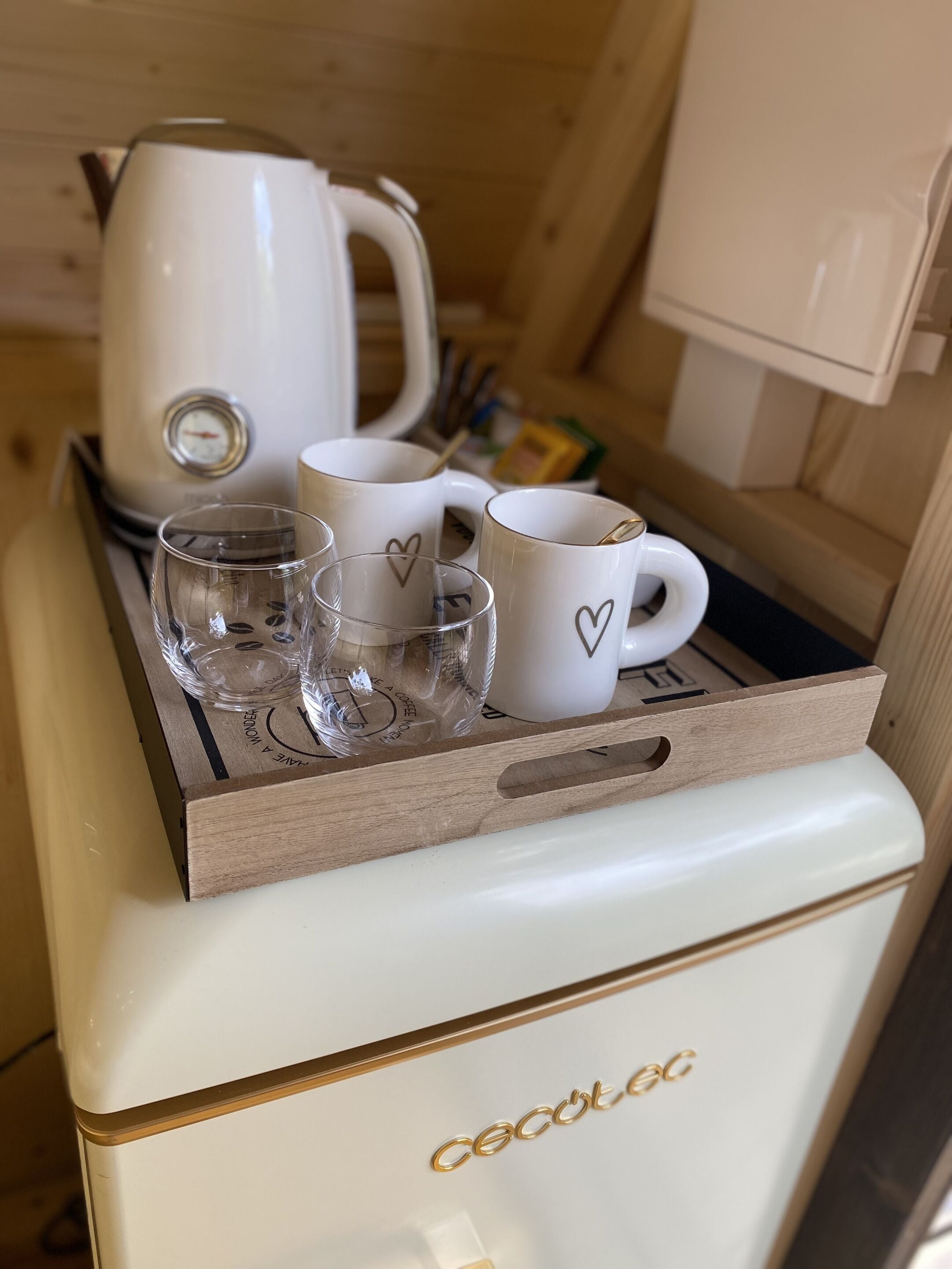 A kitchen area with a coffee maker, four white mugs with heart designs, and a glass.