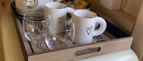 A kitchen area with a coffee maker, four white mugs with heart designs, and a glass.