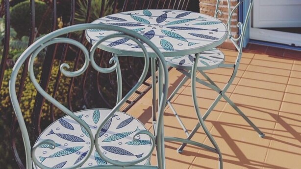 Un balcon avec une table et des chaises, une vue sur un paysage montagneux et un mur en briques.