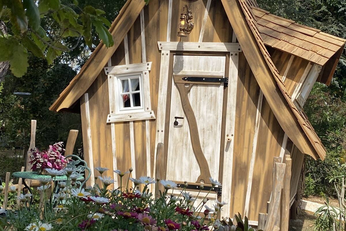 A wooden house with a triangular roof, a circular window, and a door with a black handle.