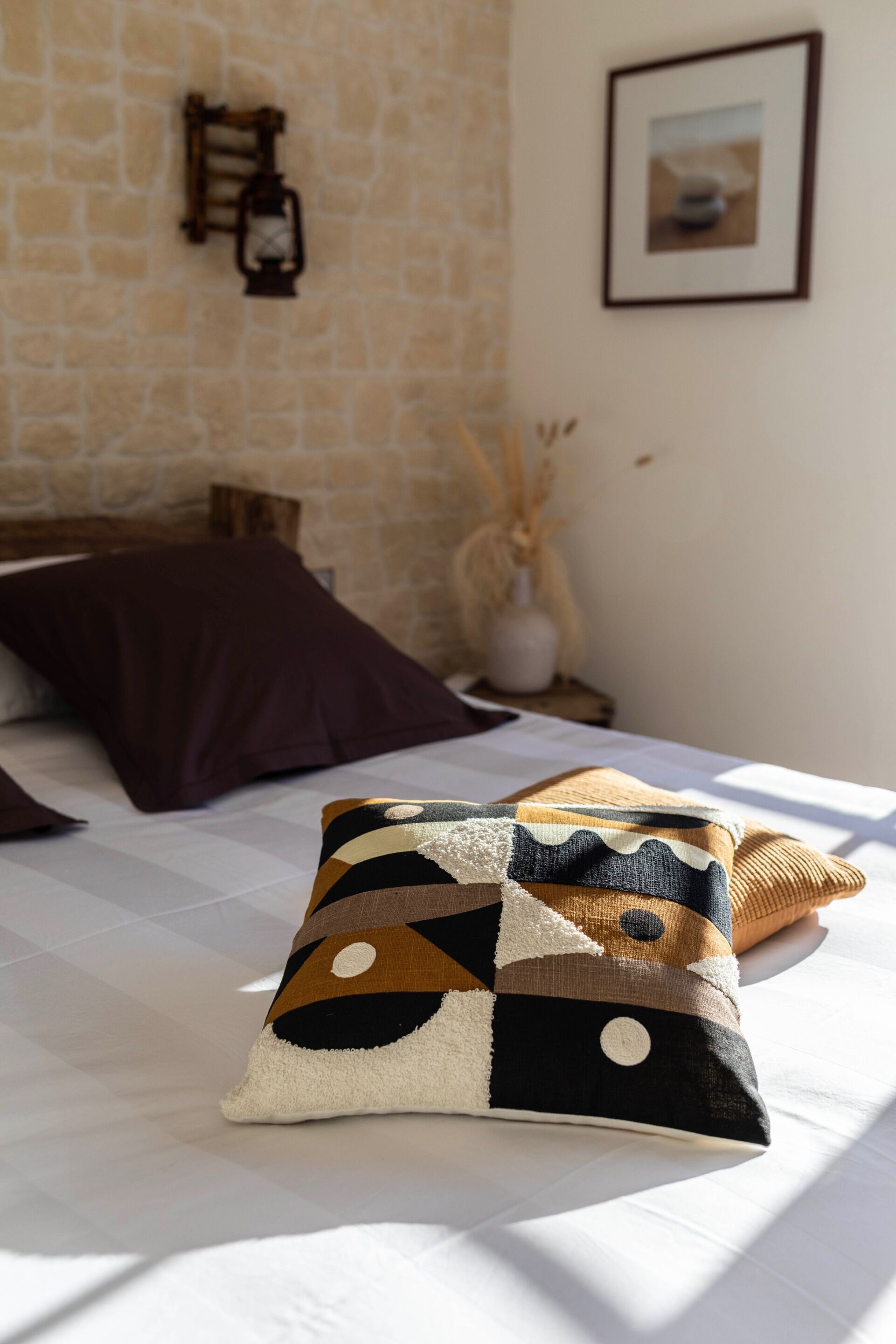A bed with a patterned pillow, a wooden headboard, and a stone wall.