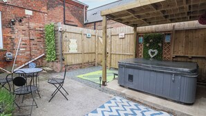 A backyard with a wooden deck, a hot tub, a patio table with chairs, and a brick wall. - The Old Station House (Withernsea)