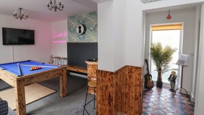 A pool table, a bar area, a neon sign, a clock, and a 'Be our guest' sign in a room with wooden accents and a tiled floor. - The Old Station House (Withernsea)