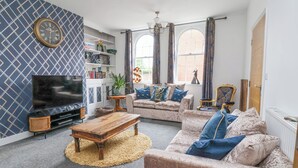 A living room with a television, sofas, a coffee table, and a patterned wall. - The Old Station House (Withernsea)