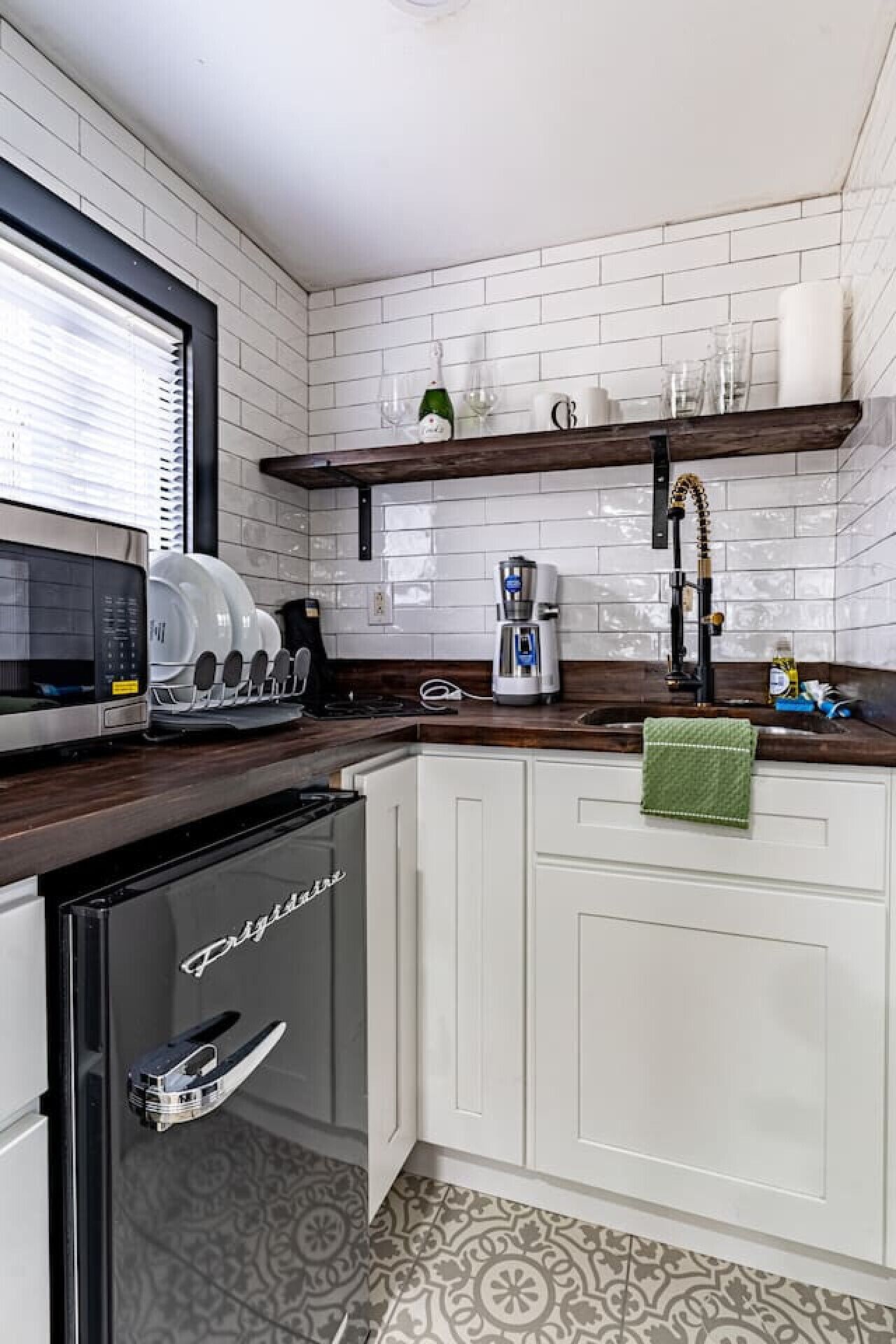 A compact kitchen with white cabinets, a built-in dishwasher, a coffee maker, and a wine bottle on a shelf.