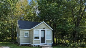 A small, single-story house with a dark front door, white trim, and a small porch. - Cozy Cabin in a Rural Setting #16 near Temple,NH (Temple)