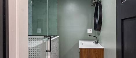 Un baño pequeño con cabina de ducha de vidrio, tocador de madera y un aplique de pared.
