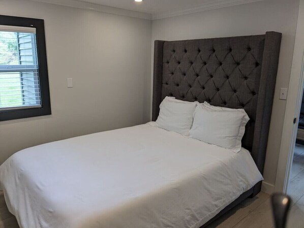 A bedroom with a large bed, a tufted headboard, and a window with blinds.