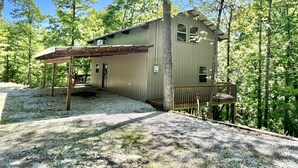 A rustic cabin with a metal exterior, a wooden porch, and a gravel driveway surrounded by trees. - Hideaway Cabin (Mountain View)