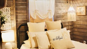A cozy bedroom with a wooden ceiling, a bed with multiple pillows, a bedside lamp, and a hanging light fixture. - Hideaway Cabin (Mountain View)