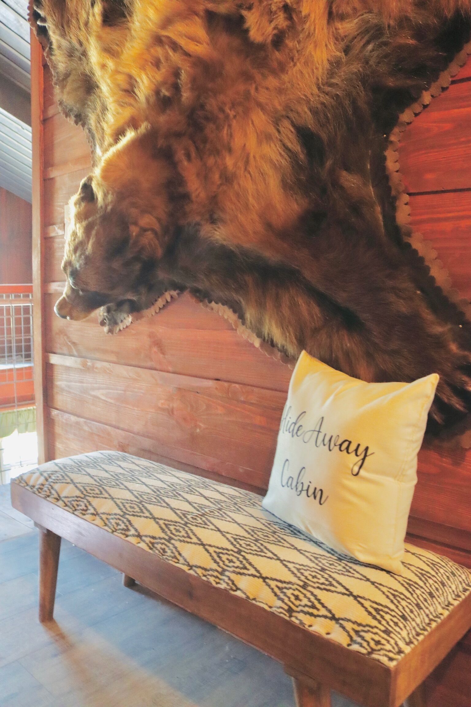 L’intérieur d’un chalet en bois, avec une tête d’animal empaillée accrochée au mur et un coussin orné de l’inscription « Slide Away Cabin ».