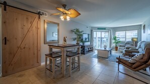 Een ruime woonkamer met een eettafel, een bank, een televisie en een plafondventilator.