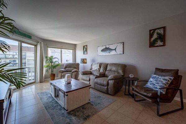 A spacious living room with a sofa, armchairs, and a coffee table. There is a large window providing natural light and a view of the outside. - Canalfront 2 Bed/2 Bath-Pvt Balcony-Sleeps 4-WiFi (Ocean City)
