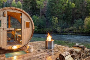A wooden cabin with a glass door, a fire pit, and a view of a river. - The River House: San Miguel Sanctuary (Telluride)