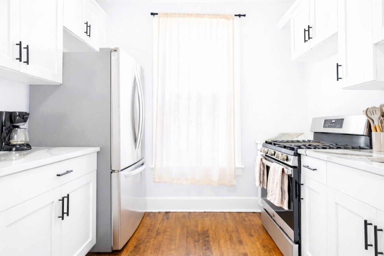 A kitchen with white cabinets, a refrigerator, a stove, and a coffee maker.