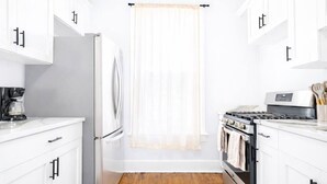 Una cocina con armarios blancos, un refrigerador, una estufa y una cafetera.