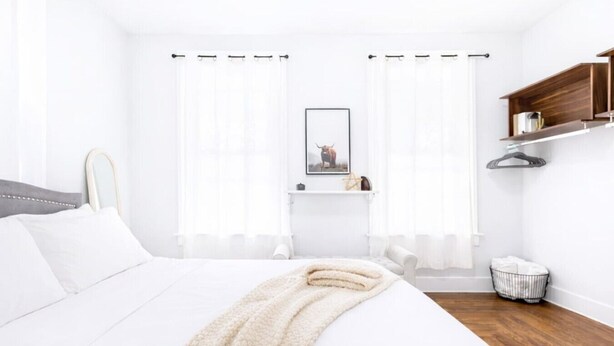Un dormitorio moderno con una cama grande, una mesita de noche, una lámpara colgante y una ventana con cortinas de gasa.