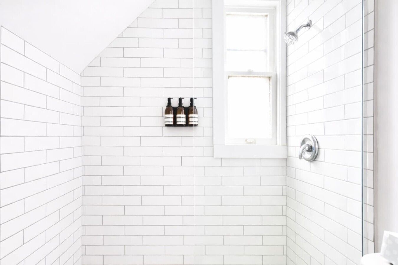 Un baño con paredes de azulejos blancos, zona de ducha y ventana.