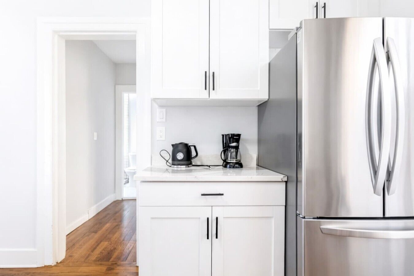 A modern kitchen with white cabinets, a stainless steel refrigerator, and a coffee maker on the countertop.