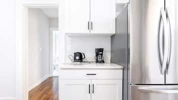 A modern kitchen with white cabinets, a stainless steel refrigerator, and a coffee maker on the countertop.