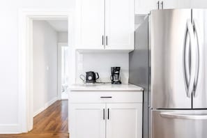 A modern kitchen with white cabinets, a stainless steel refrigerator, and a coffee maker on the countertop.