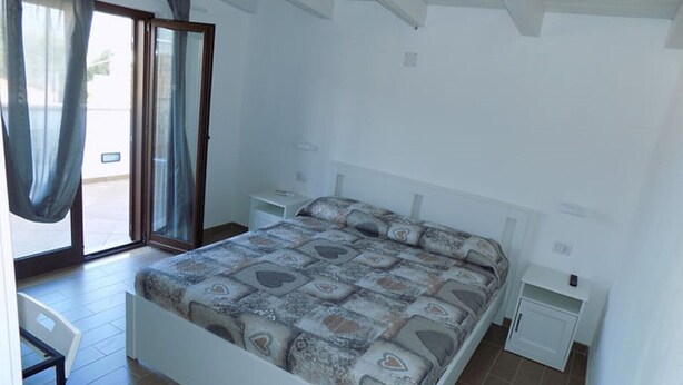 A bedroom with a bed, a nightstand, a chair, a sliding glass door, and a small table. - SEA HOUSE KAMARATON (Marina di Camerota)