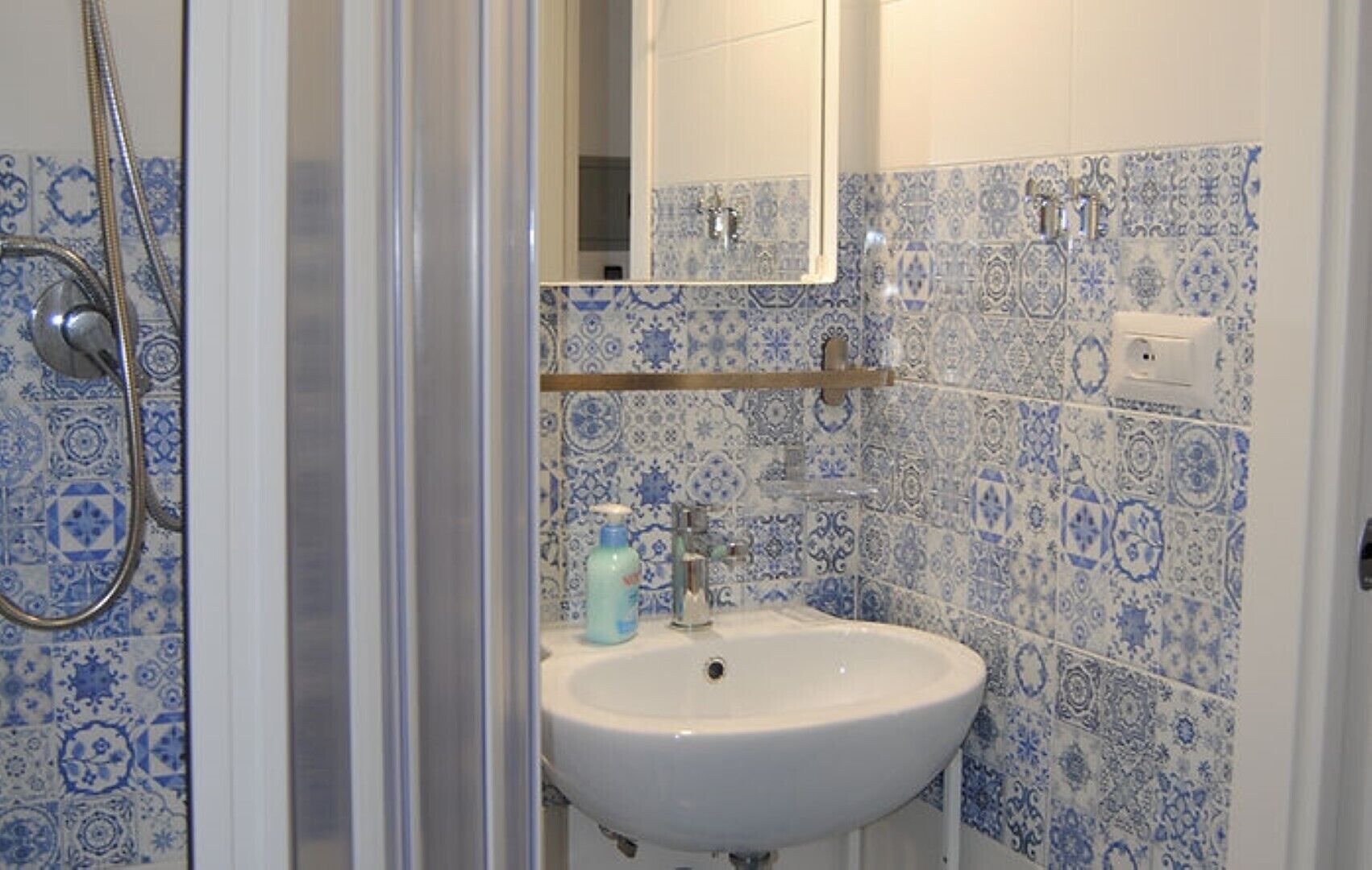 A bathroom with a white sink, blue patterned tiles, a shower, and a mirror.