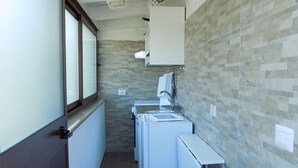 A narrow hallway with a window on the left, a tiled wall, and a washing machine and dryer on the right. - SEA HOUSE KAMARATON (Marina di Camerota)