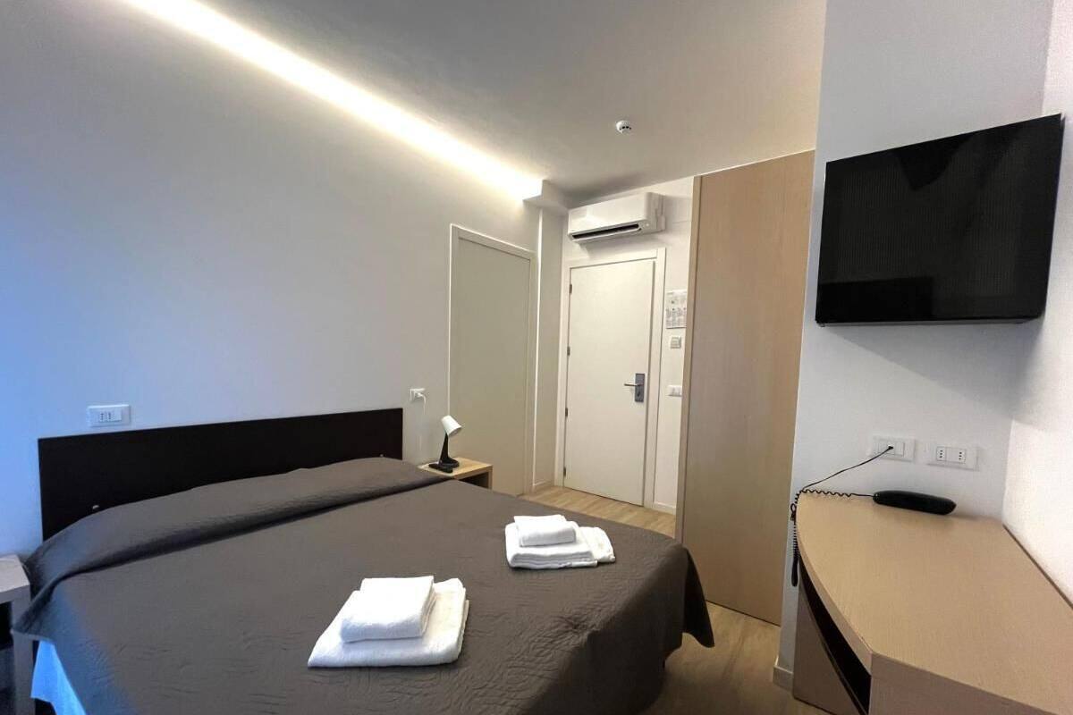 A hotel room with a large bed, a desk with a flat-screen TV, and a door leading to a bathroom.