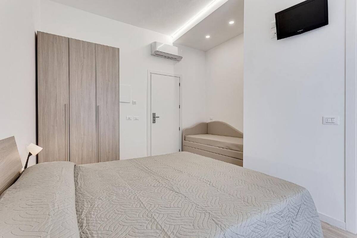 A bedroom with a bed, a wardrobe, a sofa, a TV, and an air conditioning unit.