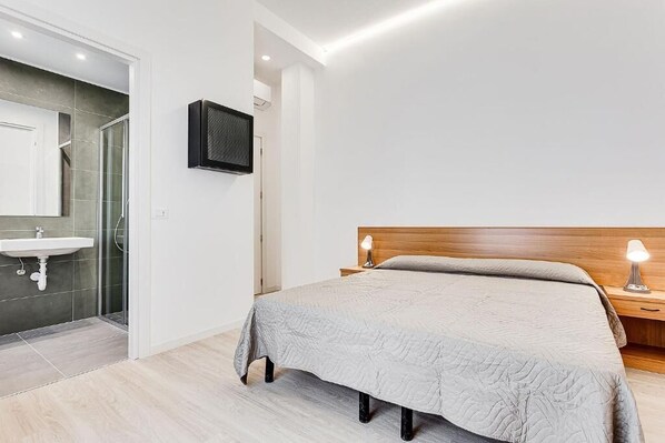 A modern bedroom with a bed, bedside lamps, a TV, and a bathroom with a sink and shower.
