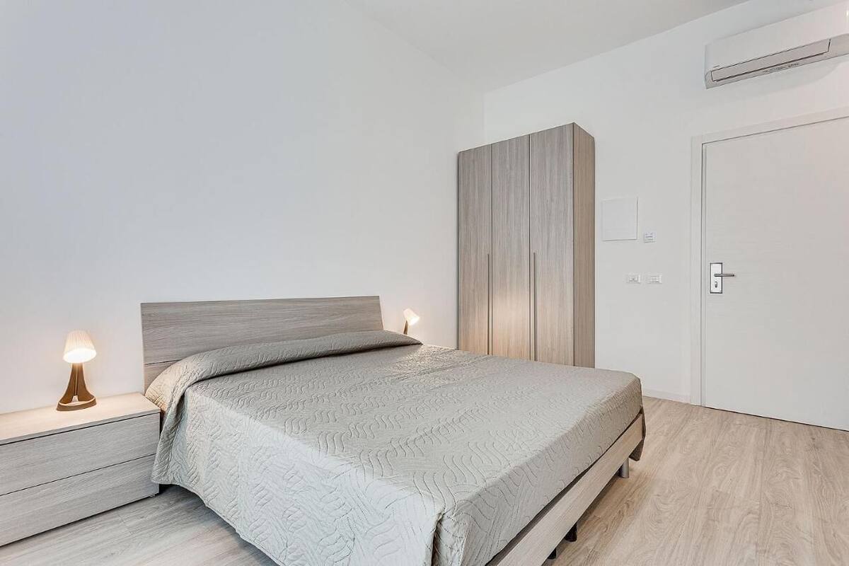 A bedroom with a bed, nightstands, a wardrobe, and an air conditioning unit.