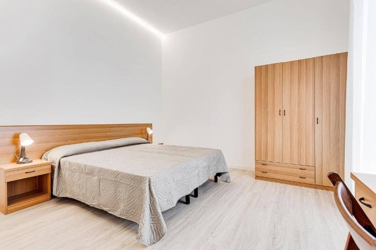 A bedroom with a bed, wooden nightstand, bedside lamp, and a wooden wardrobe.