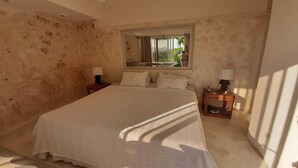A bedroom with a large bed, two bedside tables, a window with a view, and a mirror on the wall.