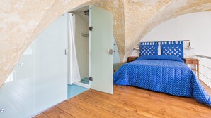 Un dormitorio con techo inclinado, una cama con ropa de cama azul y una zona de ducha.