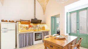 Una cocina con mesa de madera, sillas, refrigerador, horno y salpicadero de azulejos.