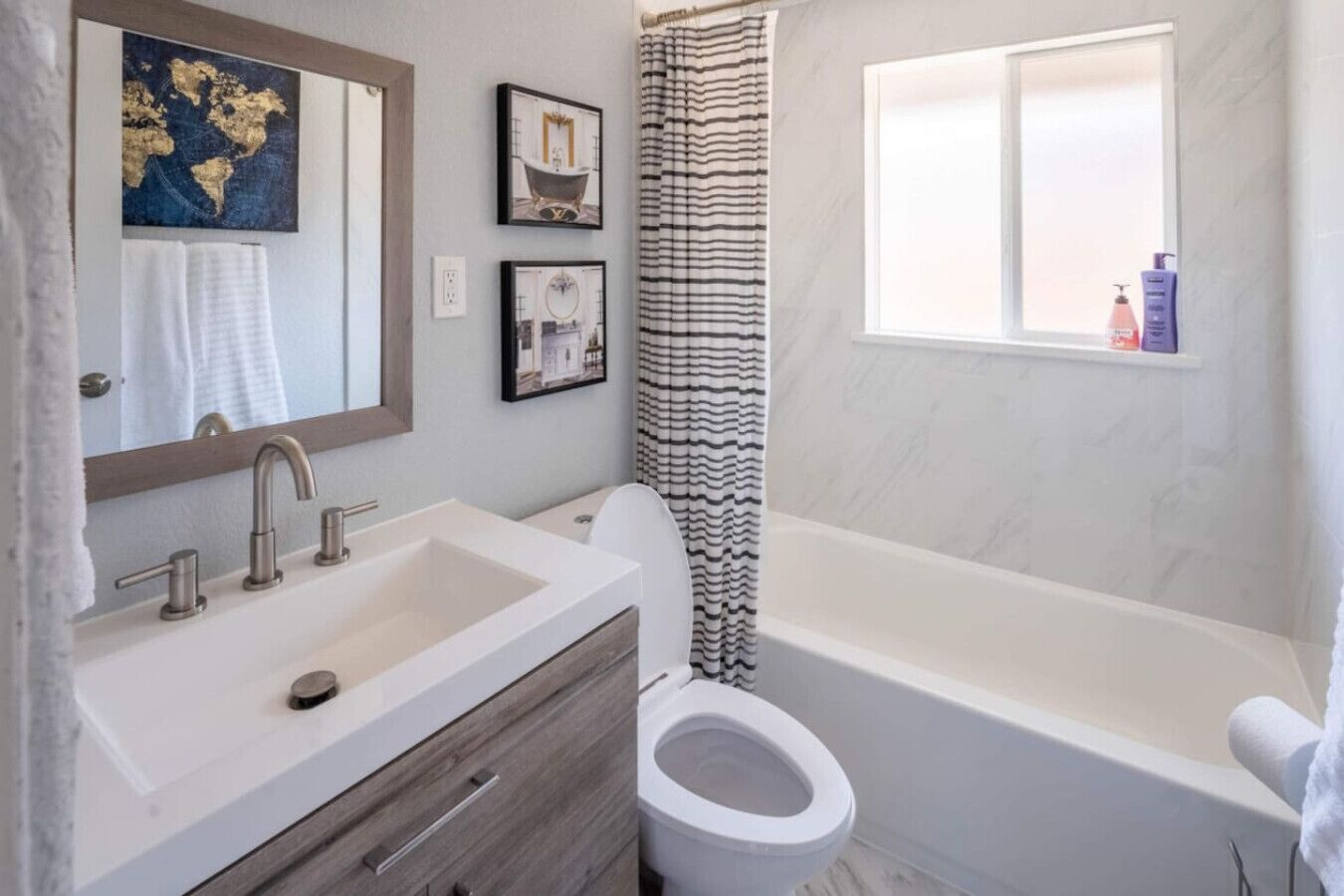 Ein Badezimmer mit einem großen Waschbecken, Toilette und Badewanne. An der Wand hängen Bilder in Rahmen und über der Badewanne befindet sich ein Fenster.