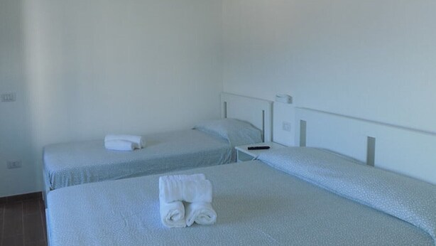 Une chambre avec deux lits simples, chacun doté d’un matelas et d’une tête de lit blancs. Des serviettes sont soigneusement pliées sur les lits.