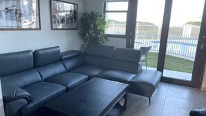 Una sala de estar moderna con un sofá modular, una mesa de centro y un amplio ventanal con vista a un área exterior cercada.