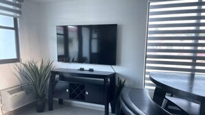 Un salón moderno con un televisor de pantalla plana montado en la pared, una mesa de centro de madera oscura, un banco y una planta en maceta.