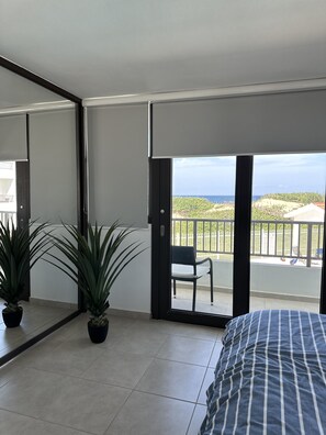 A bedroom with a large bed, a sliding glass door leading to a balcony with a view of the sea and greenery. - Villa Luna at Marbela Casa de Playa (Isabela)