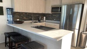 Una cocina moderna con una isla grande, electrodomésticos de acero inoxidable y taburetes de bar de madera.