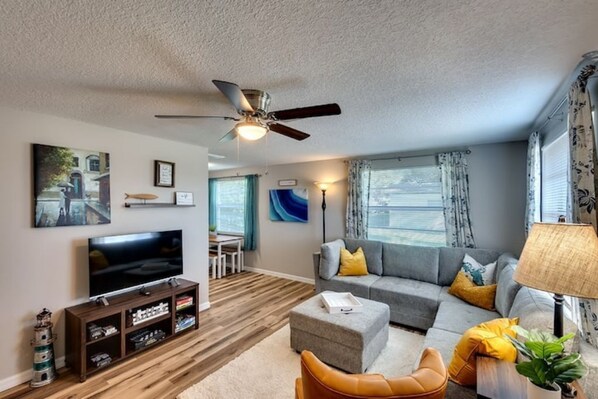 A modern living room with a flat-screen TV, a ceiling fan, a sofa set, and a coffee table.