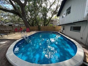 Piscina com deck de madeira, cercada por um muro de madeira e árvores.