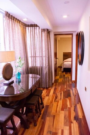 Un comedor con mesa y sillas de madera, un florero con planta y una ventana con cortinas.