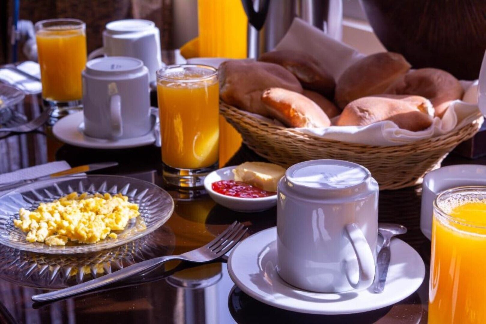Une table dressée pour le petit-déjeuner avec des œufs brouillés, du jus d’orange, des croissants et une tasse de café.