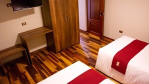 Habitación de hotel con dos camas, un banco de madera, un armario y un televisor en la pared.