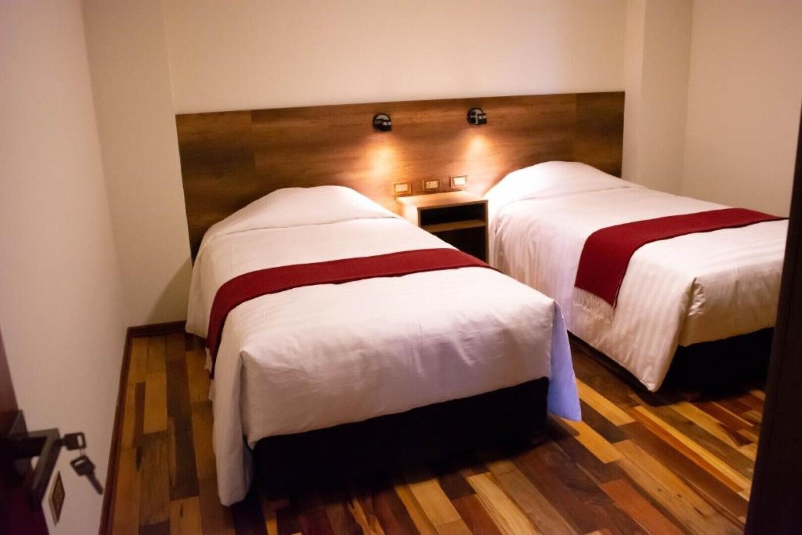 Une chambre avec deux lits, une tête de lit en bois et une petite table de chevet avec des lampes.