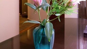 Eine blaue Vase mit einer rosa Blume und grünem Blattwerk auf einer dunklen Oberfläche in einem Flur.